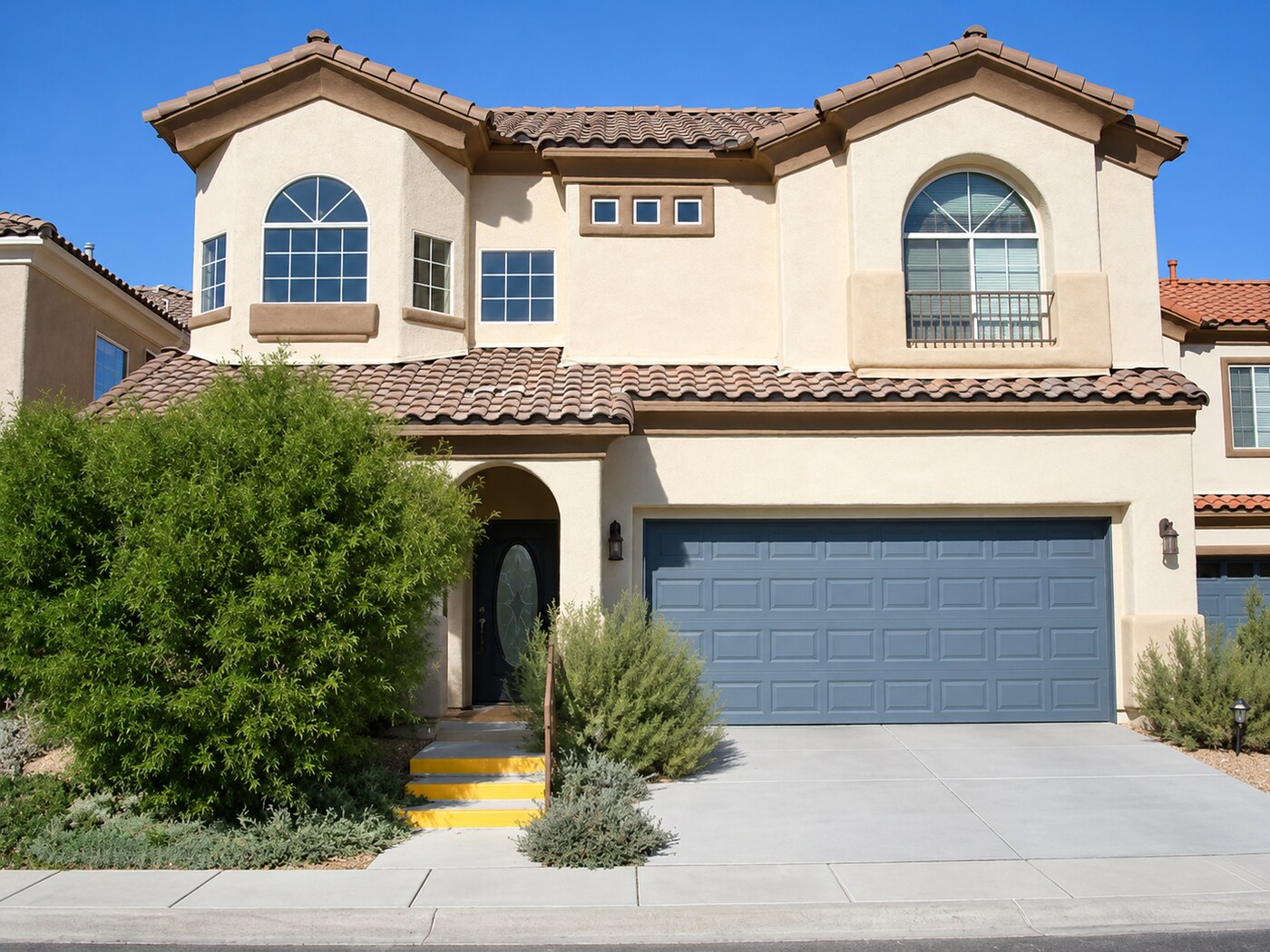 Two-story Mediterranean-style home with arched windows and a blue garage door
